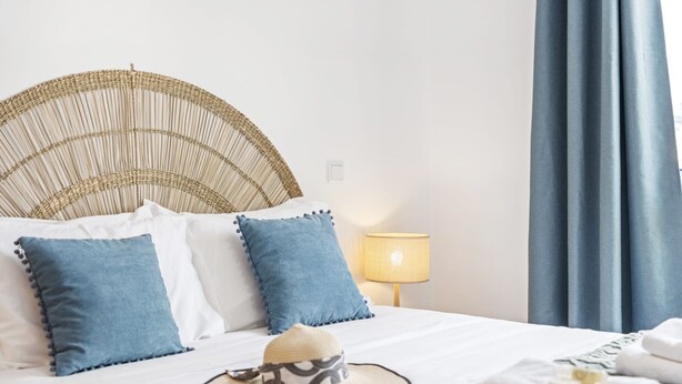 A neatly made bed with blue and white pillows, a straw hat, and folded towels. - Locally by Homie in Funchal (Funchal)