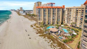 A beachfront hotel with multiple high-rise buildings, a sandy beach, and a swimming pool area.
