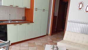 A kitchen with light green cabinets, a white countertop, and a tiled floor. There is a white sofa and a small white table with decorative items. - BELVEDERE - Bed & Breakfast - Holiday Home (Pozzilli)