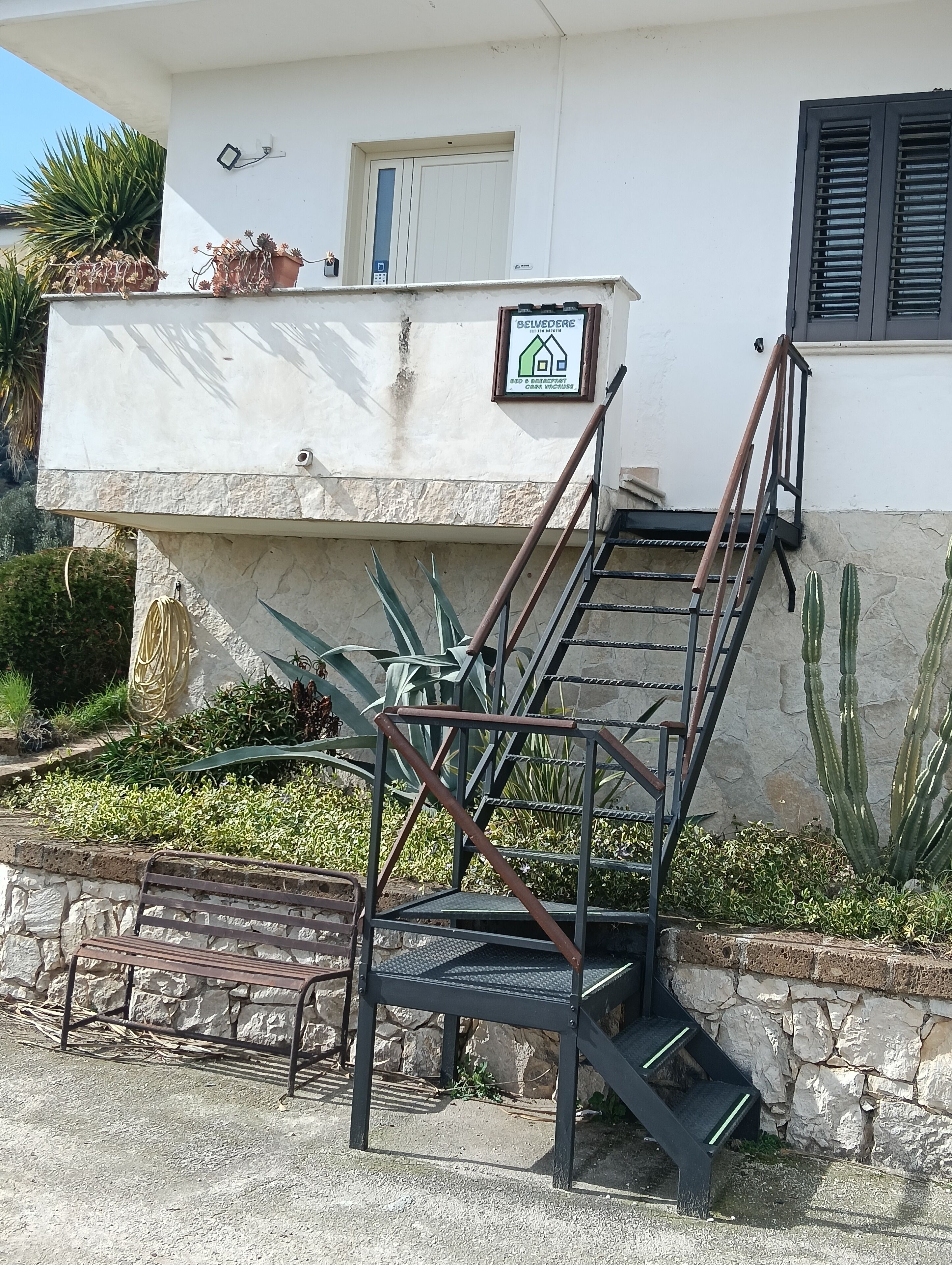 Eine Treppe führt zu einem Gebäude mit einem Schild, umgeben von Pflanzen und einer Steinmauer.