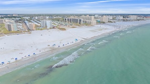 An aerial view of a beach with multiple buildings in the background, a sandy shore, and clear turquoise water. - Gulf & Bay Club Bayside | Walk to Beach, Enjoy Pools, Tennis & More (Siesta Key)