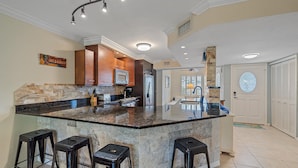 A spacious kitchen with a large island, dark countertops, and wooden cabinets. - Gulf & Bay Club Bayside | Walk to Beach, Enjoy Pools, Tennis & More (Siesta Key)