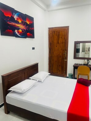 A bedroom with a wooden bed, a red bedspread, a wooden door, a desk with a chair, and a wall-mounted mirror. - Hotel Ceylonia Colombo  (Colombo)