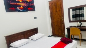 A hotel room with a bed, a wooden door, a desk with a chair, and a wall-mounted mirror. - Hotel Ceylonia Colombo (Colombo)