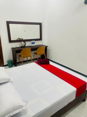 Una habitación de hotel con una cama, un escritorio con dos sillas, un espejo y un corredor rojo.