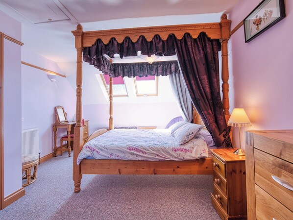 A four-poster bed with a canopy, a wooden dresser, a bedside lamp, and a framed picture on the wall.