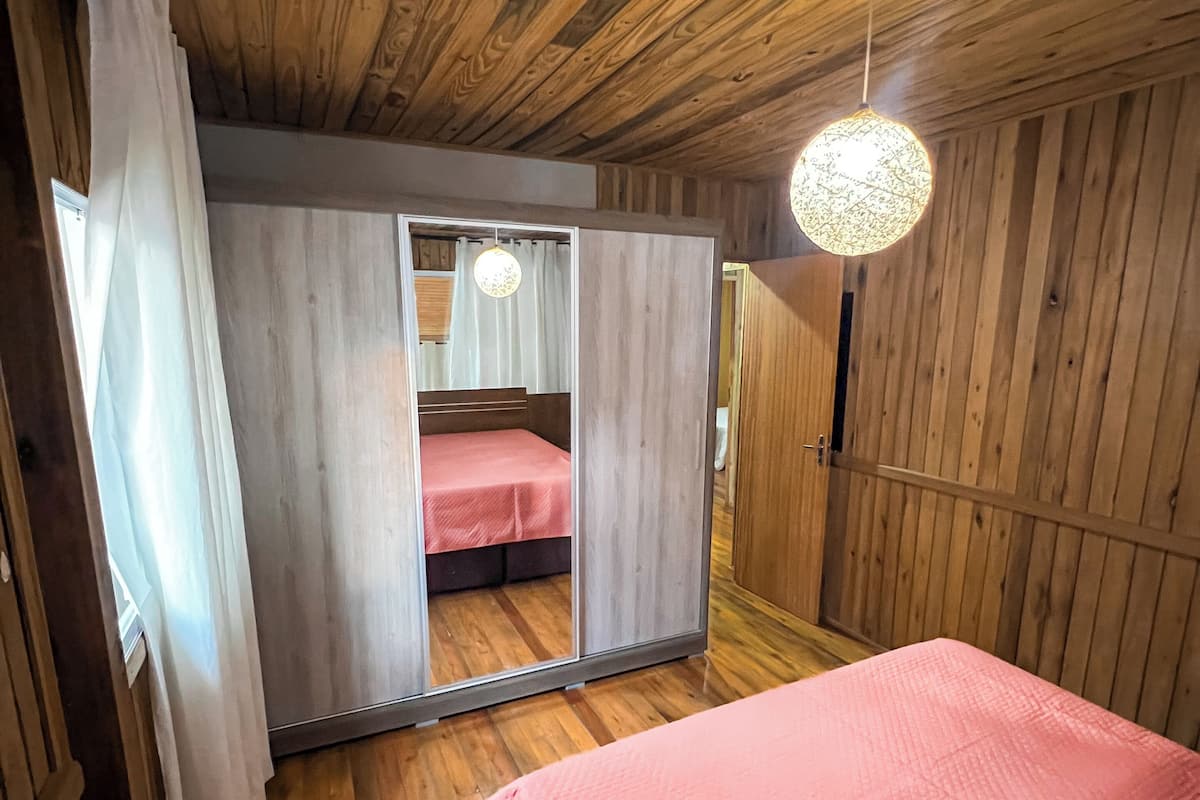 A wooden room with a bed, a mirror, and a hanging light fixture.