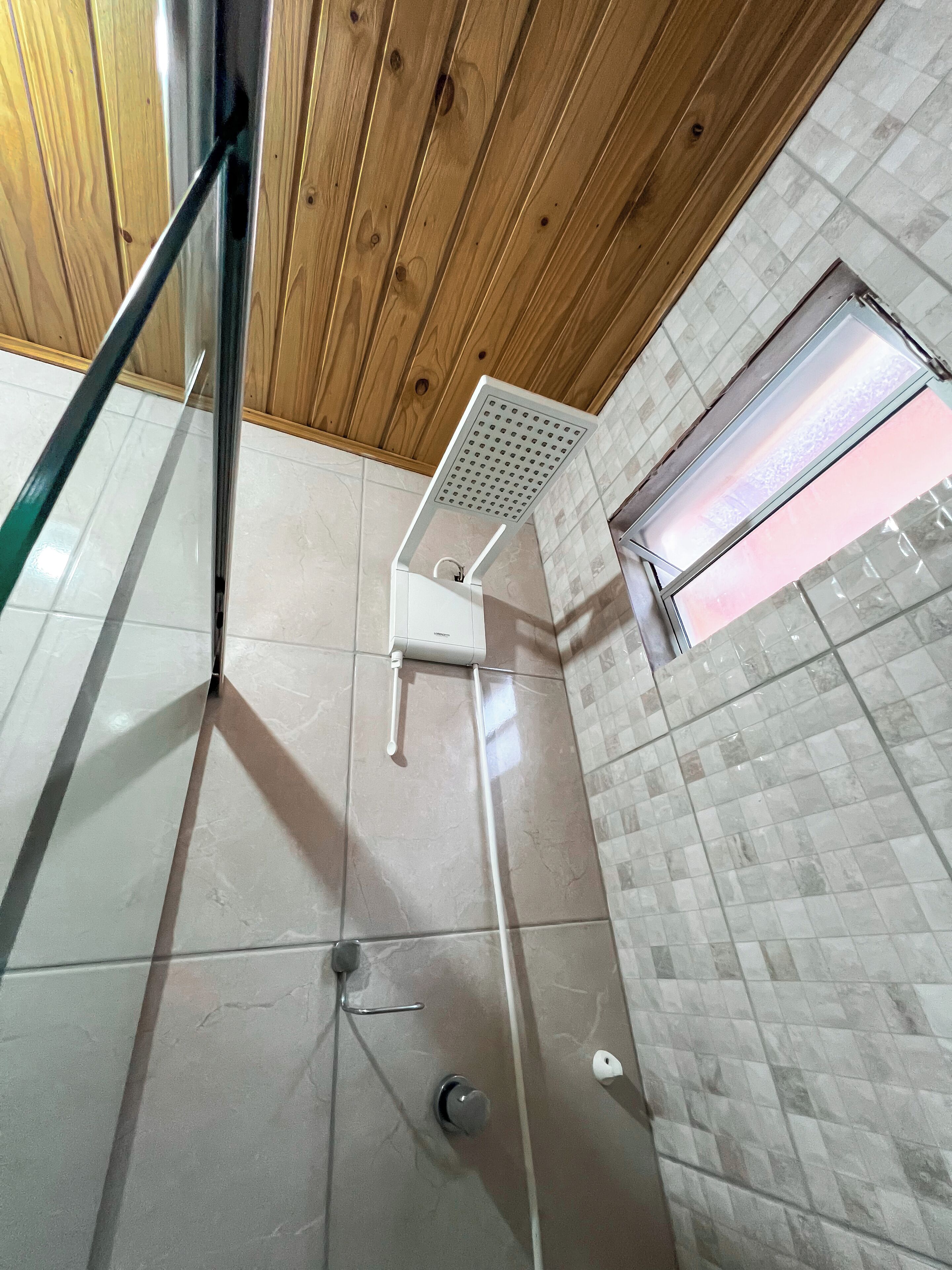 Un espacio de ducha con puerta de cristal, un cabezal de ducha manual blanco y una pared con azulejos.