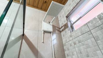 Un espacio de ducha con puerta de cristal, un cabezal de ducha manual blanco y una pared con azulejos.