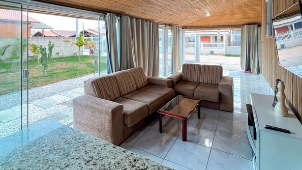 A spacious living room with a wooden ceiling, a sectional sofa, a coffee table, and large windows offering a view of the outside.