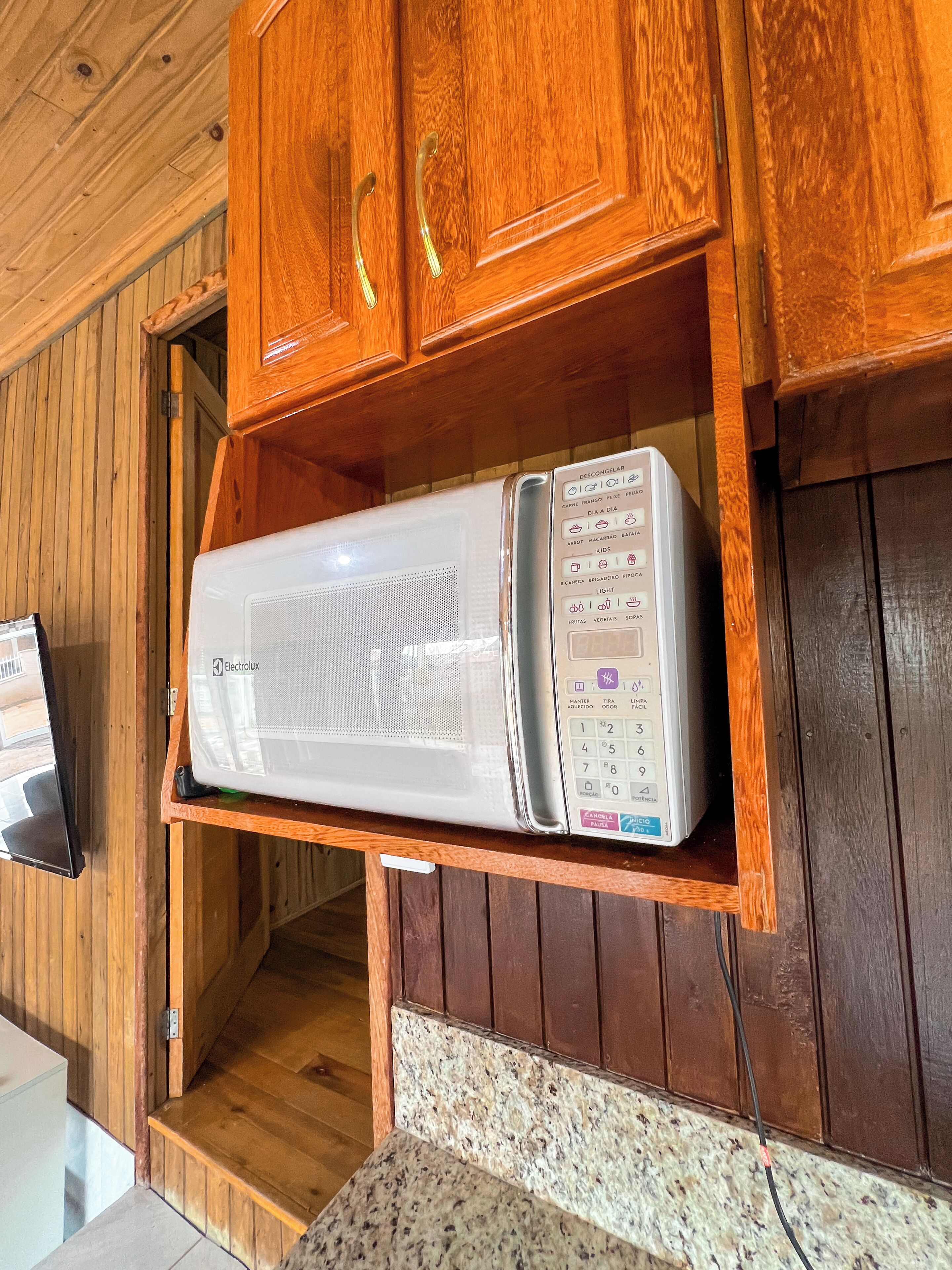 Un horno microondas sobre una repisa de madera en una cocina con paredes de madera y una encimera de granito.