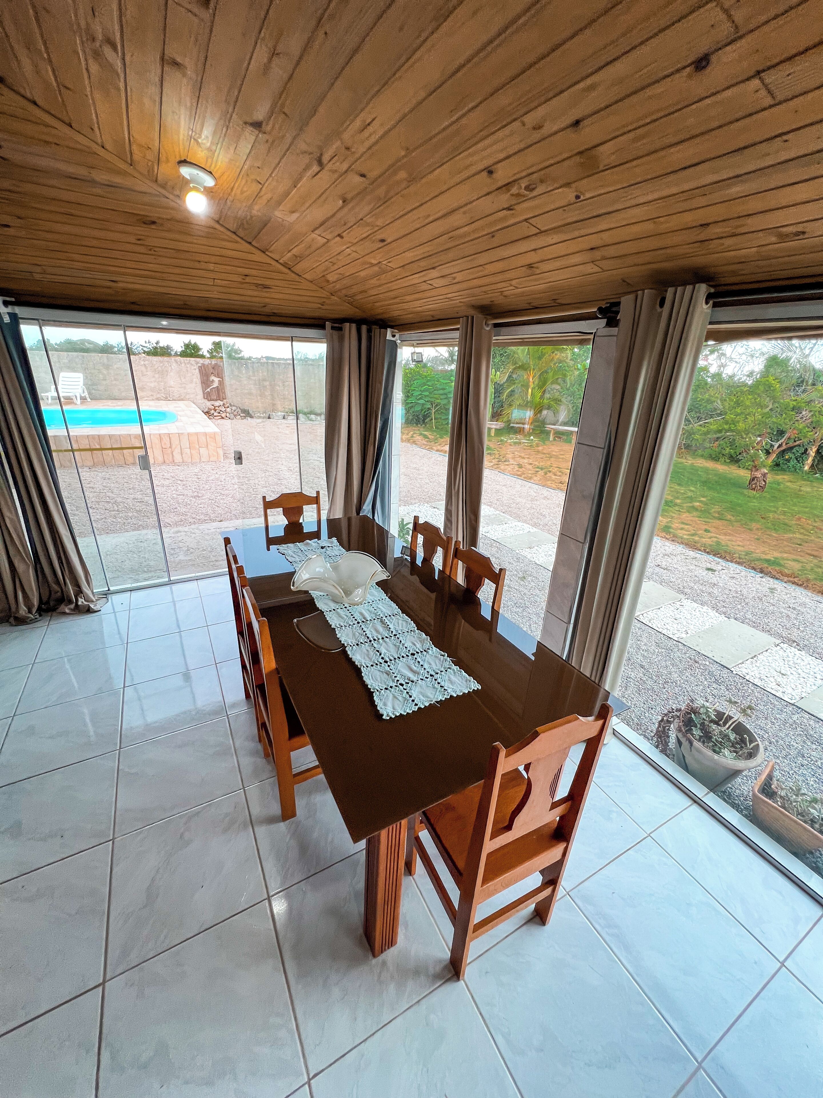 Un espace repas avec une table et des chaises en bois, de grandes fenêtres et une vue sur une piscine extérieure.