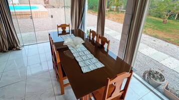 Un espace repas avec une table et des chaises en bois, de grandes fenêtres et une vue sur une piscine extérieure.