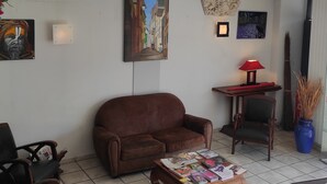 Un salon avec un canapé marron, une table basse sur laquelle sont posés des magazines, une lampe rouge et un tableau représentant une scène de rue.