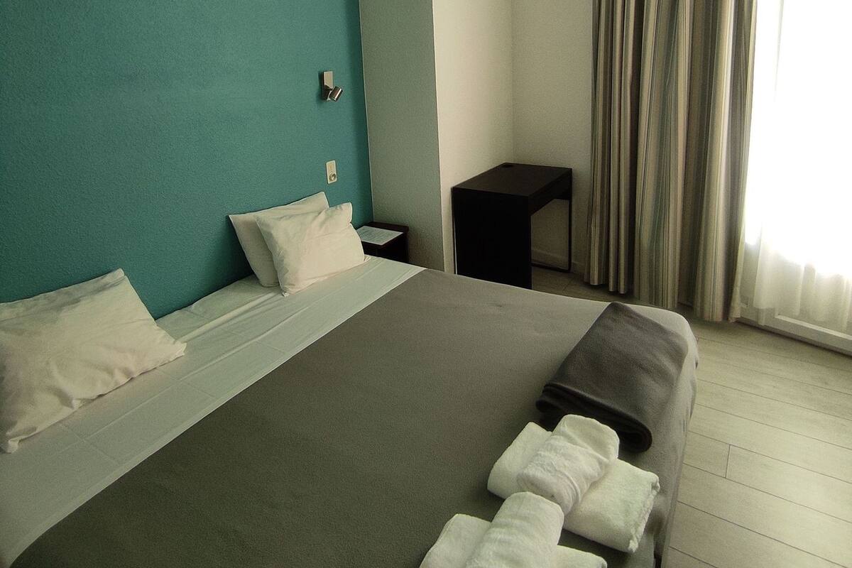 Ein Hotelzimmer mit Bett, Kissen, einem kleinen Tisch und einem Vorhang.