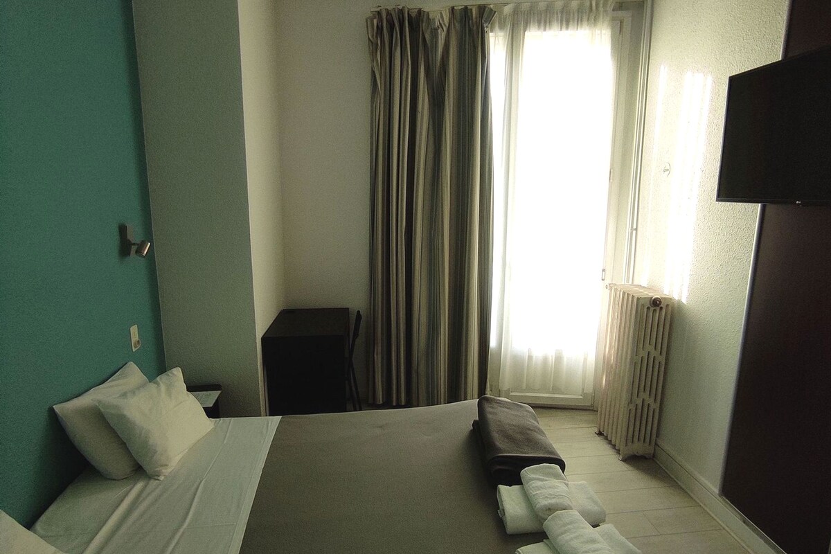 Une chambre d’hôtel avec un lit, des oreillers, un banc, un bureau et un radiateur.