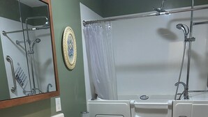 A bathroom with a white sink, wooden vanity, a toilet, a bathtub with a showerhead, and a blue trash bin. - Charming 3-bedroom house in Mountain City beautiful big coy pond in backyard (Mountain City)