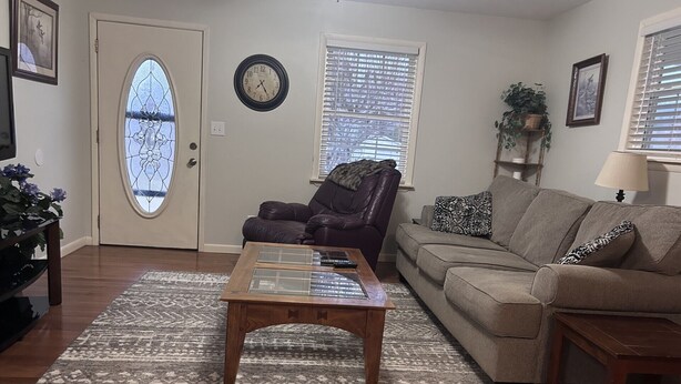 A living room with a wooden coffee table, two sofas, a decorative rug, a door with a stained glass window, and a wall clock. - Charming 3-bedroom house in Mountain City beautiful big coy pond in backyard (Mountain City)