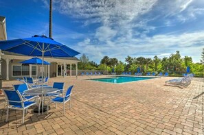 Ein Poolbereich mit blauen Stühlen, Sonnenschirmen, einem Pool und einer Ziegelterrasse.