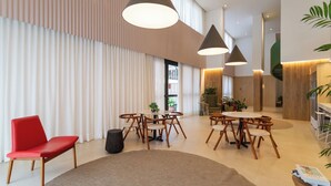 A modern hotel lobby with a large seating area, wooden tables, and hanging pendant lights. - Co.Next Liberdade (Sao Paulo)