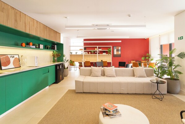 A modern hotel lobby with a green reception desk, a beige sofa, and a red accent wall. - Co.Next Liberdade (Sao Paulo)