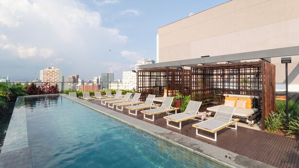 A rooftop infinity pool with lounge chairs and a wooden pergola. - Co.Next Liberdade (Sao Paulo)