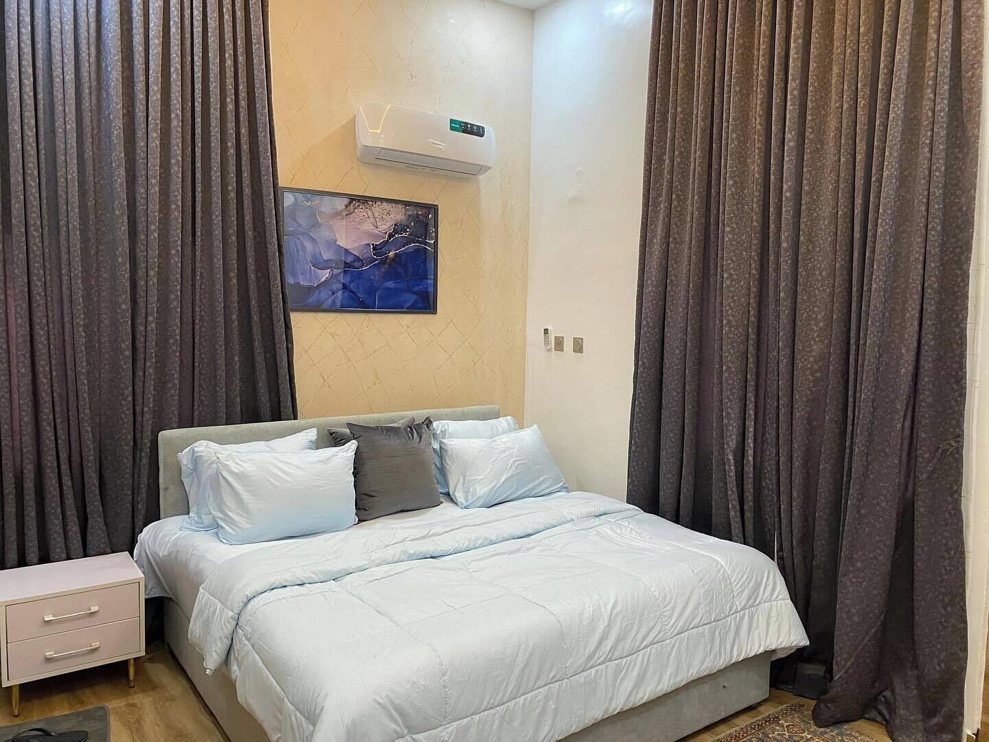Une chambre à coucher comprenant un lit, une table de chevet, un climatiseur fixé au mur et un tableau.