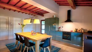 A modern kitchen with wooden beams, a dining table with chairs, and a built-in oven. - Tuscan villa for 8 people with pool near Lucca. (Borgo a Mozzano)