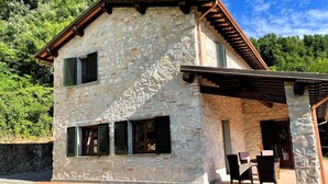 A stone building with a sloped roof, multiple windows with shutters, and a covered outdoor seating area. - Tuscan villa for 8 people with pool near Lucca. (Borgo a Mozzano)