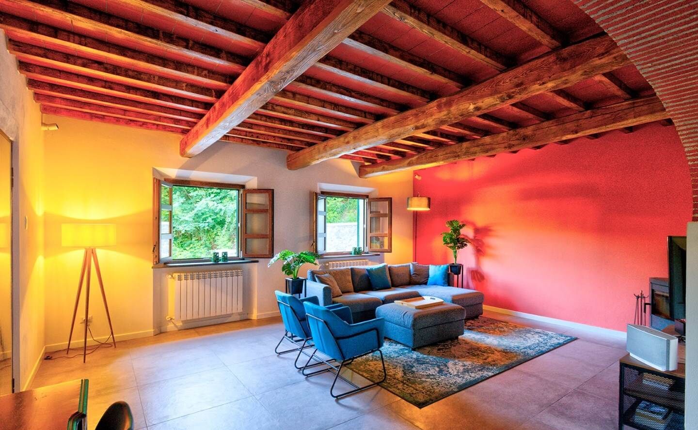 Een woonkamer met een houten plafond, een zithoek, een vloerlamp en een radiator.