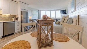 Een moderne keuken met witte kasten, een roestvrijstalen koelkast en een eethoek met een ronde tafel en geweven placemats.