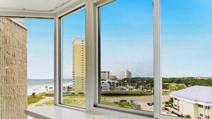 Een kamer met een groot raam met uitzicht op een strand en een stadsbeeld.
