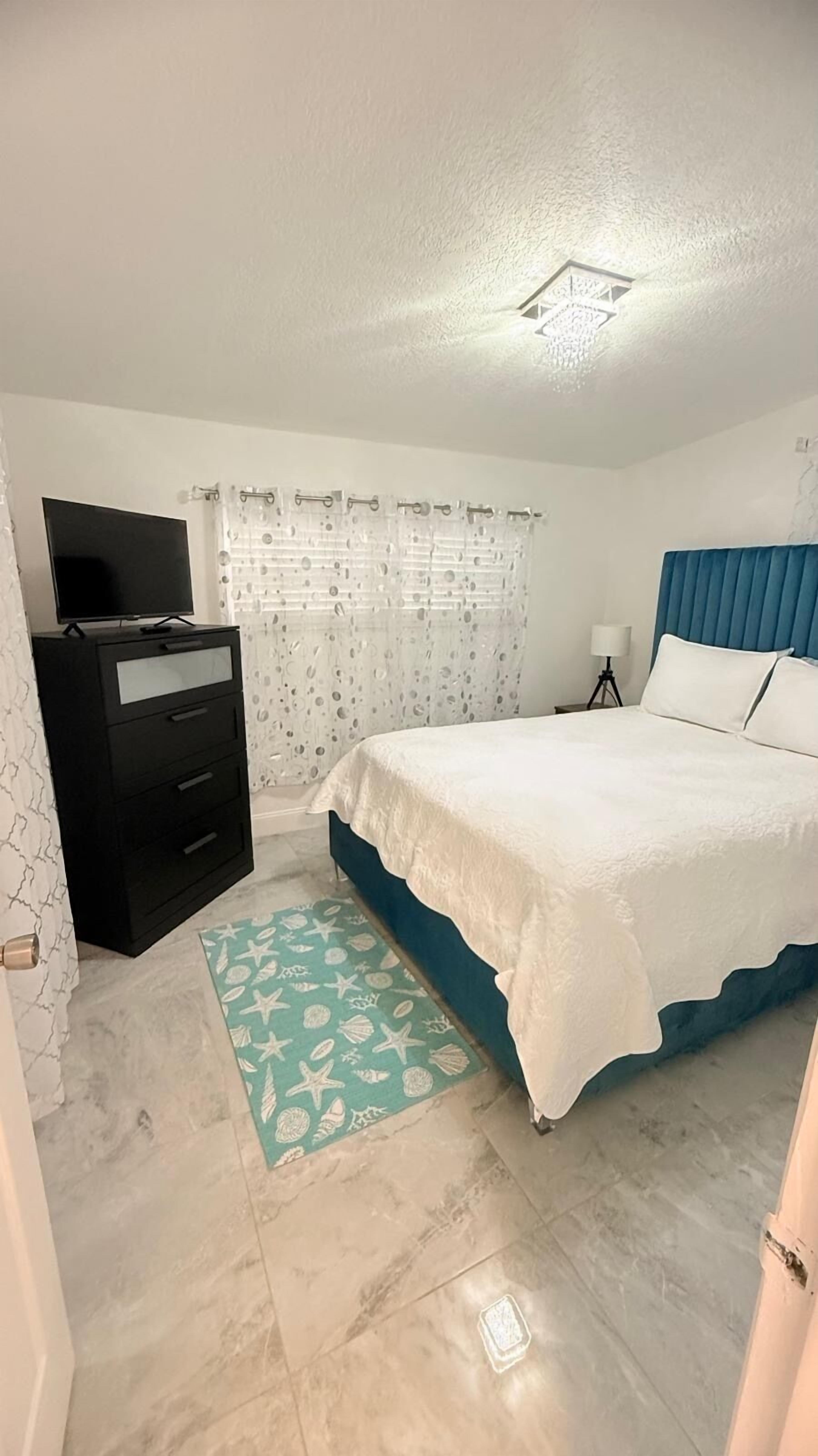 A bedroom with a bed, a dresser, a TV, and a bathroom.