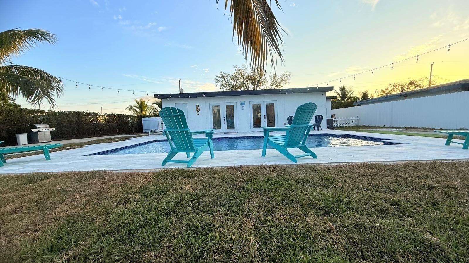 Zona de piscina con dos sillas turquesas, un edificio pequeño y una palmera.