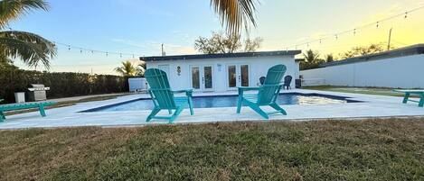 Zona de piscina con dos sillas turquesas, un edificio pequeño y una palmera.