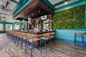A bar area with a long counter, multiple bar stools, and a green wall with a plant display.