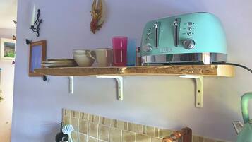 A kitchen with a teal toaster, a shelf with bowls and a pink cup, and a wall-mounted light fixture.