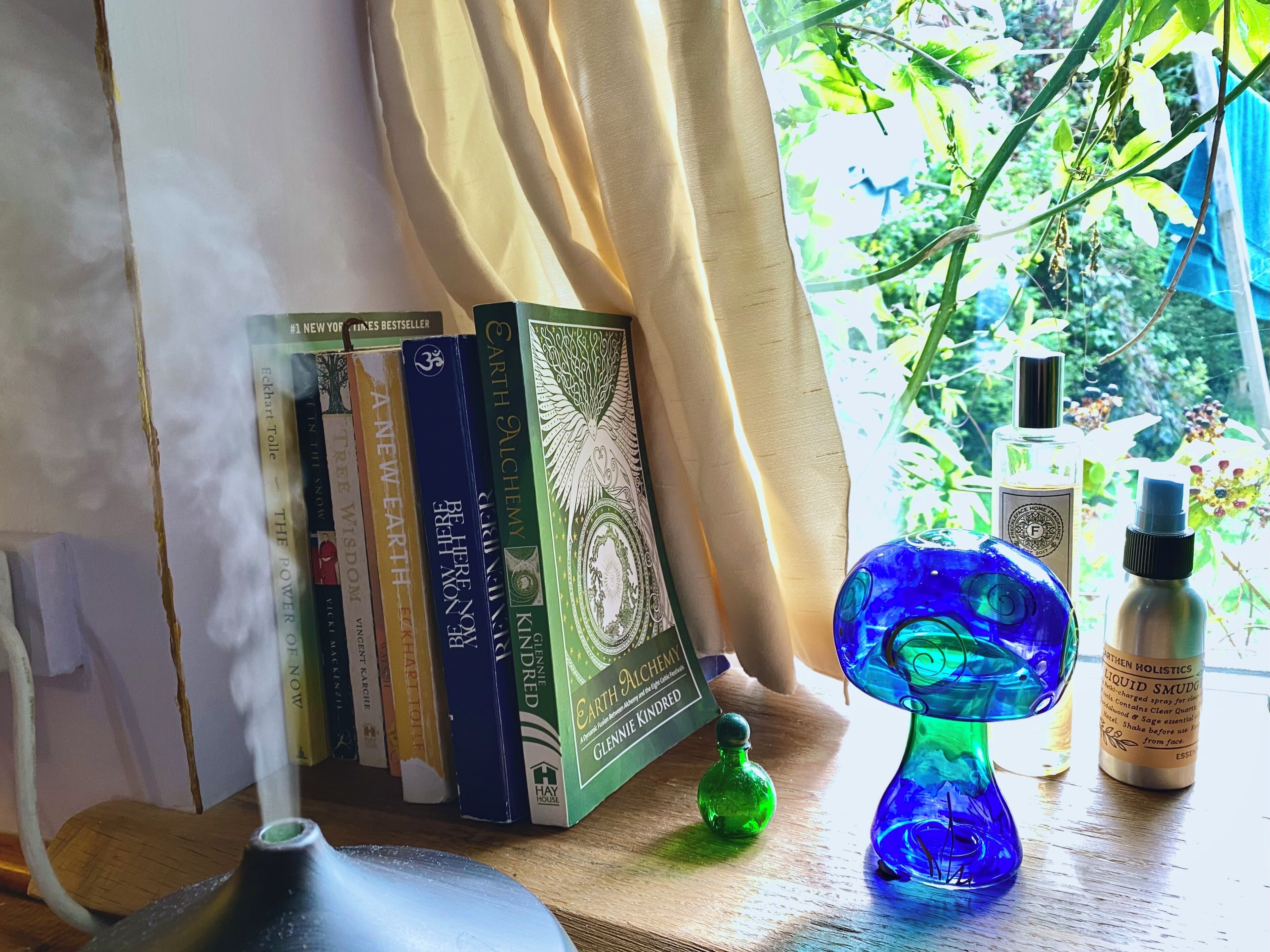 Una mensola con libri, una bottiglia di vetro verde e un vaso di vetro blu su una superficie di legno vicino a una finestra con tende.