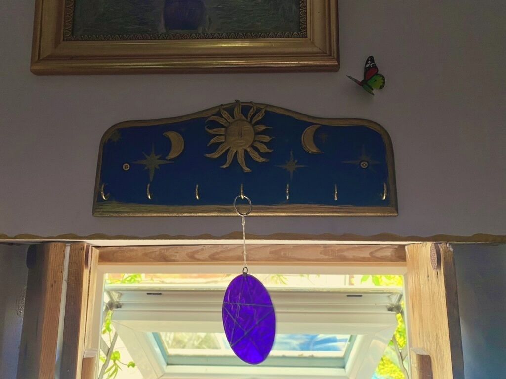 Une pièce dont le plafond est orné d’un élément décoratif représentant des motifs célestes, avec un ornement violet suspendu et un tableau encadré au-dessus.