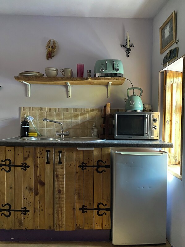 A kitchen with wooden cabinets, a microwave, a kettle, and a sink.