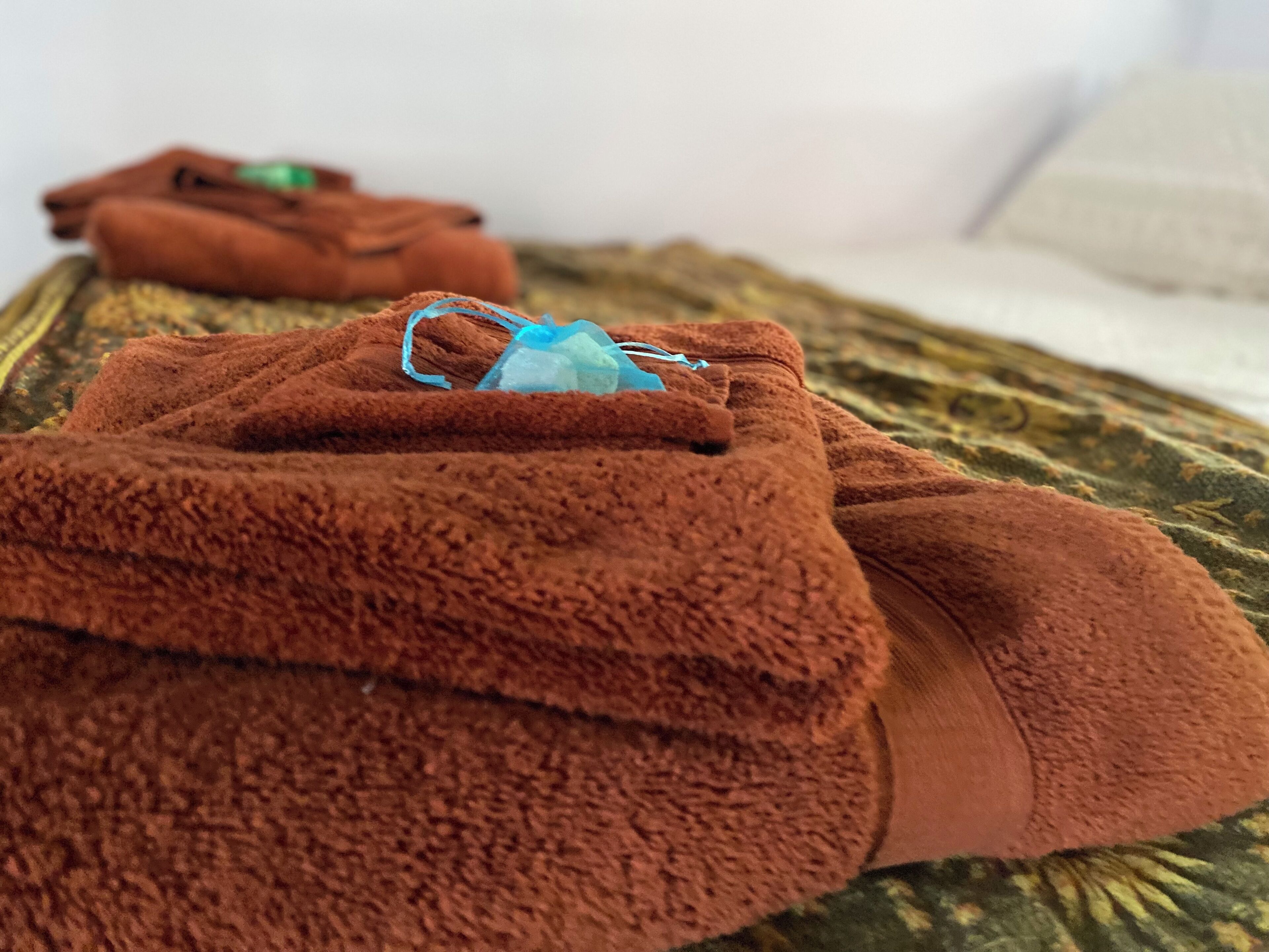 Une serviette marron sur laquelle est posé un masque pour le visage, le tout placé sur un lit recouvert d’une couvre-lit à motifs.