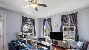 A living room with a sofa, armchair, coffee table, TV, and curtains. - Multi-Gen Retreat w/ Fenced Yard, Porches & Pet Amenities (Galveston)