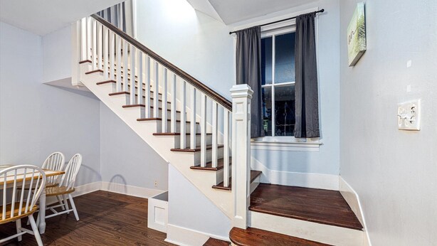 A staircase with white railings and wooden steps, leading to a room with a dining table and chairs. - Multi-Gen Retreat w/ Fenced Yard, Porches & Pet Amenities (Galveston)