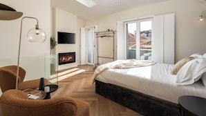 Een moderne slaapkamer met een groot bed, een open haard, een glazen salontafel en uitzicht op de stad door grote ramen.