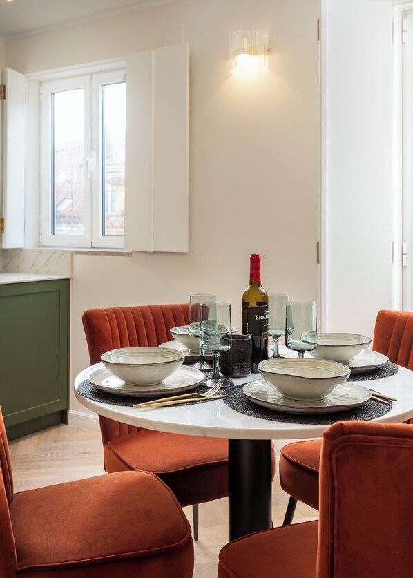A dining area with a round table set for six, surrounded by six orange chairs. A bottle of wine and several glasses are on the table.