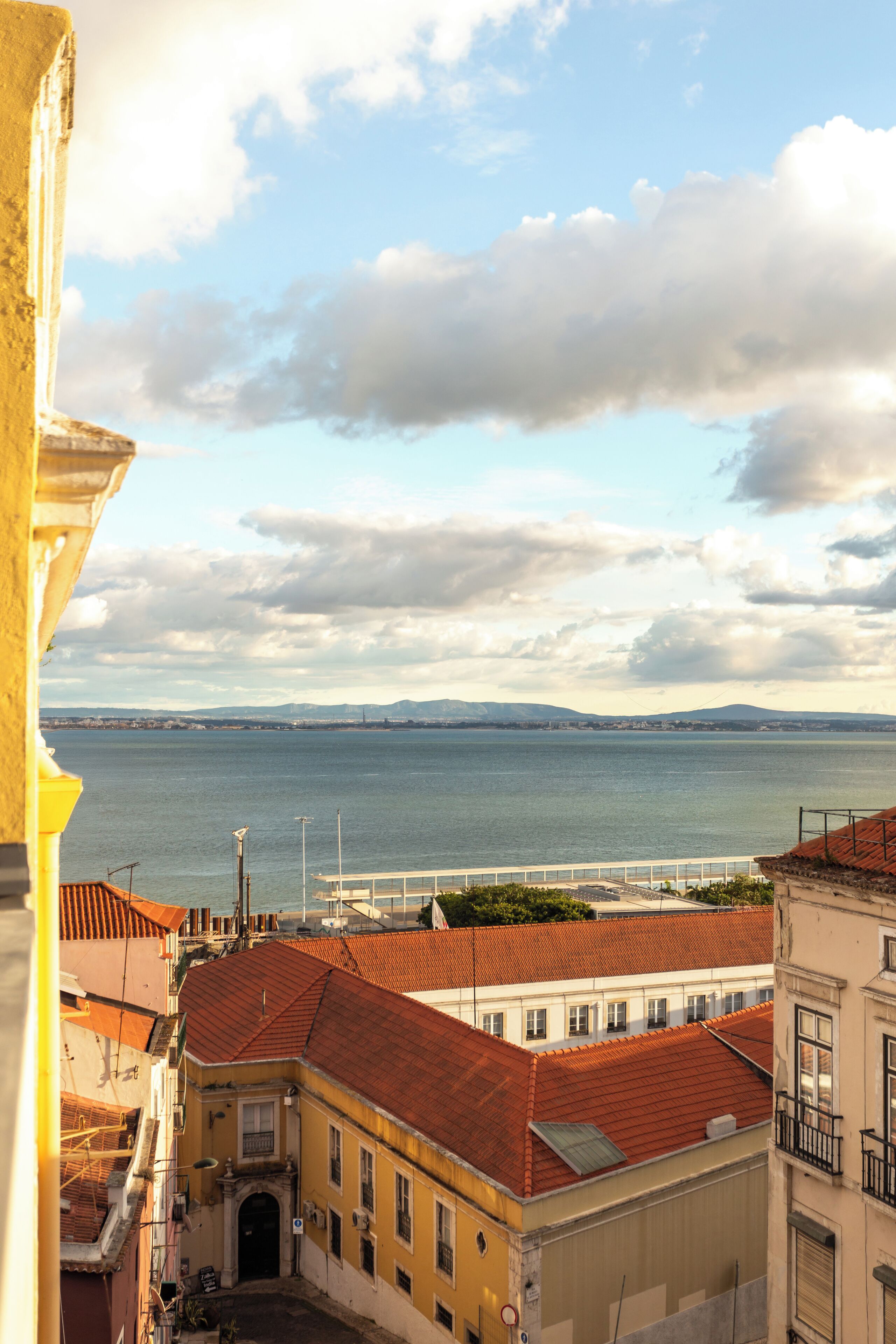 A coastal cityscape with buildings, a bridge, and a view of the sea.