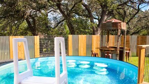 Un jardin avec une piscine, une terrasse en bois et un espace clos délimité par une structure en bois.