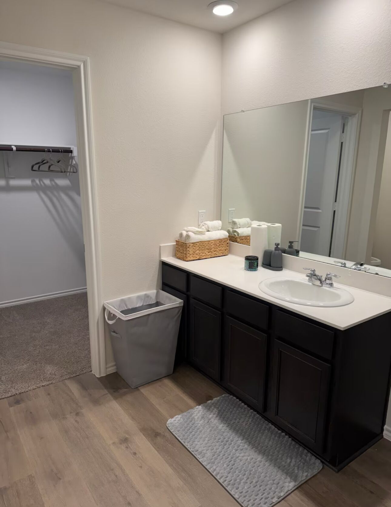 Un baño moderno con un lavamanos blanco, muebles oscuros, un espejo y un cubo de basura.
