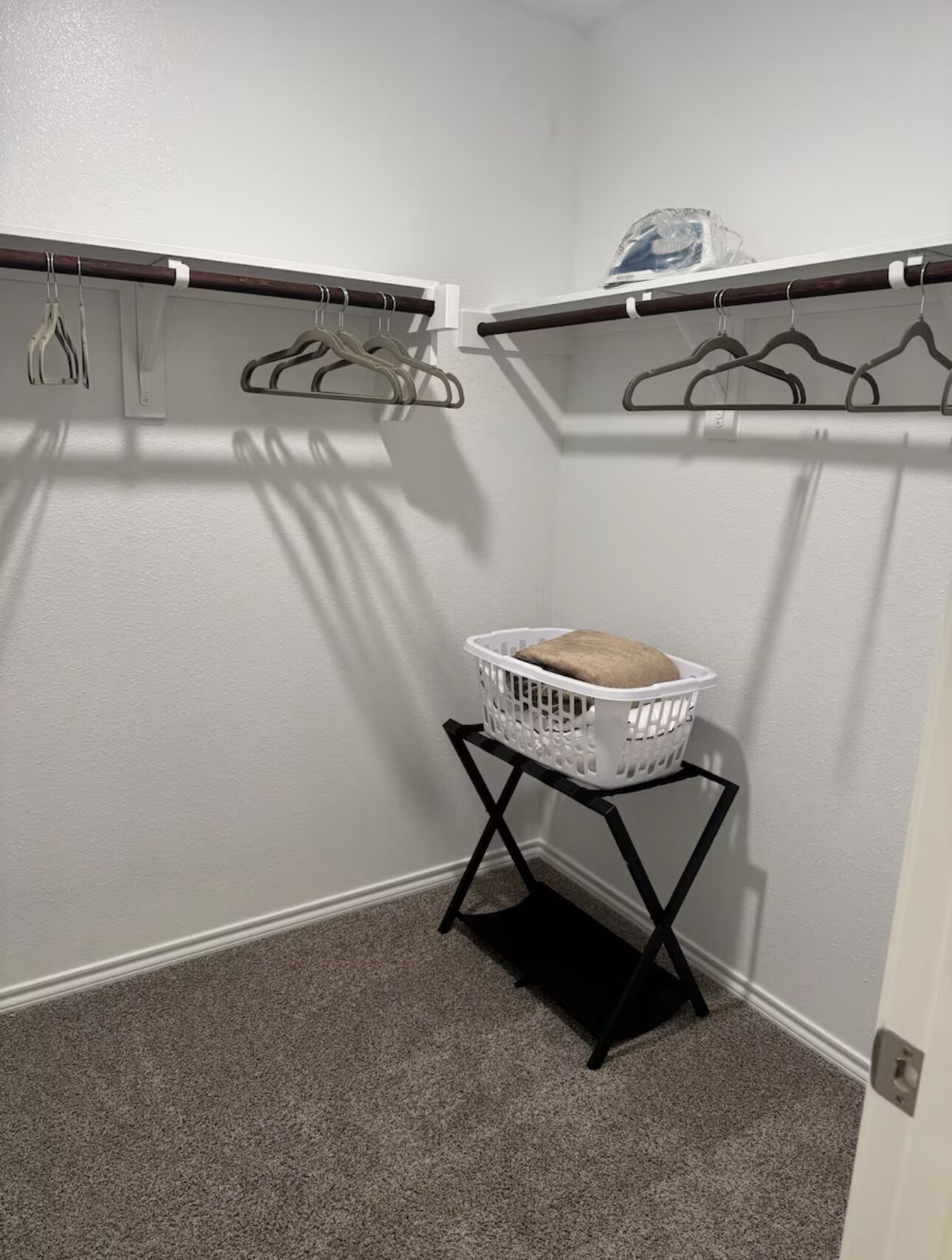 Un lavadero con una cesta blanca sobre un soporte negro, dos ganchos para abrigos en la pared y una puerta a la derecha.