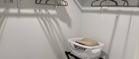 Un lavadero con una cesta blanca sobre un soporte negro, dos ganchos para abrigos en la pared y una puerta a la derecha.